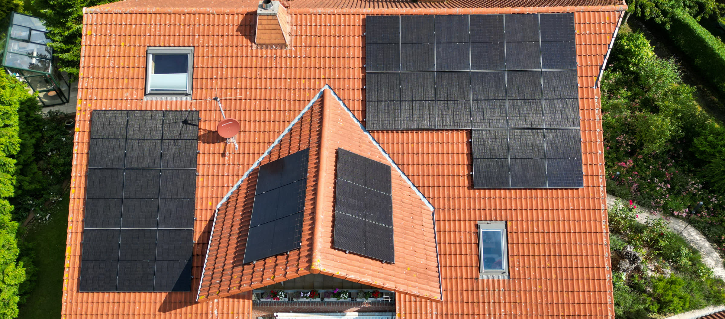 Einfamilienhaus mit rotem Ziegeldach und schwarzen Solarmodulen auf mehreren Dachflächen aus der Vogelperspektive