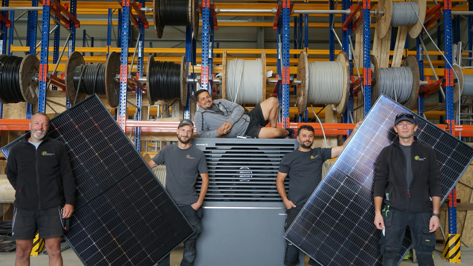 Monteure von Solarservice Norddeutschland mit einer Wärmepumpe und zwei Solarmodulen in der Lagerhalle